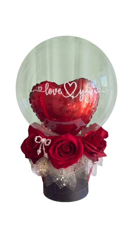 The Love Whisper Balloon Rose Box featuring premium red roses, a metallic heart balloon inside a crystal-clear bubble balloon with "Love You" text, presented in a luxury black hat box by Gifts & Co.